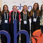 Six professionally dressed women facing the camera smiling.