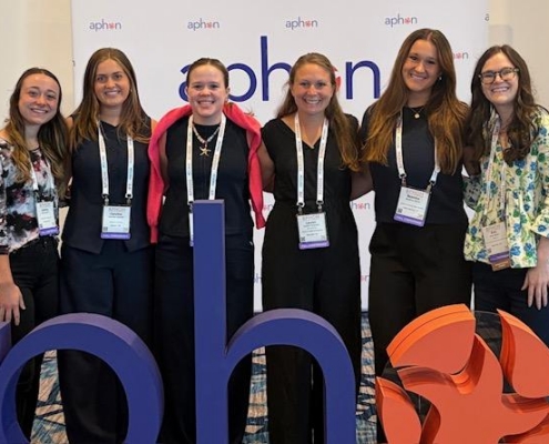 Six professionally dressed women facing the camera smiling.
