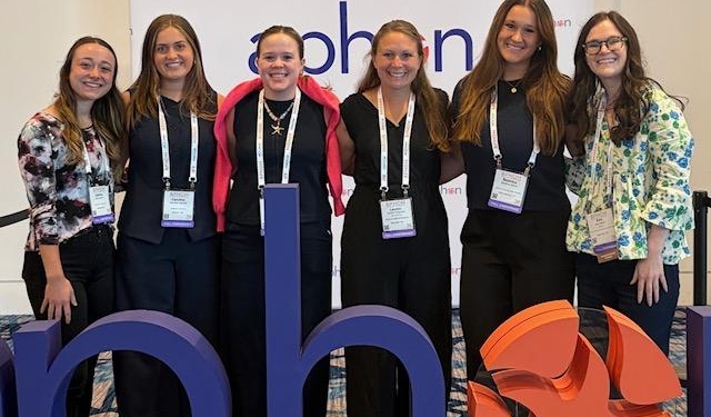 Six professionally dressed women facing the camera smiling.
